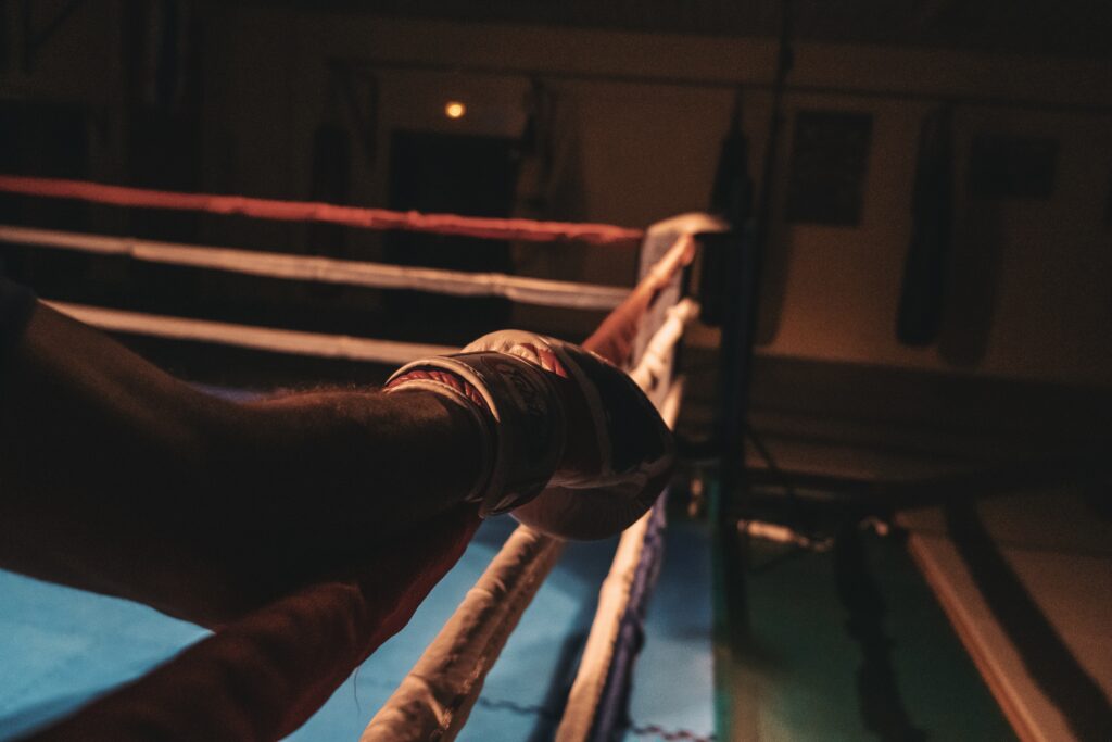 man with boxing glove resting his arm on the edge of a boxing ring